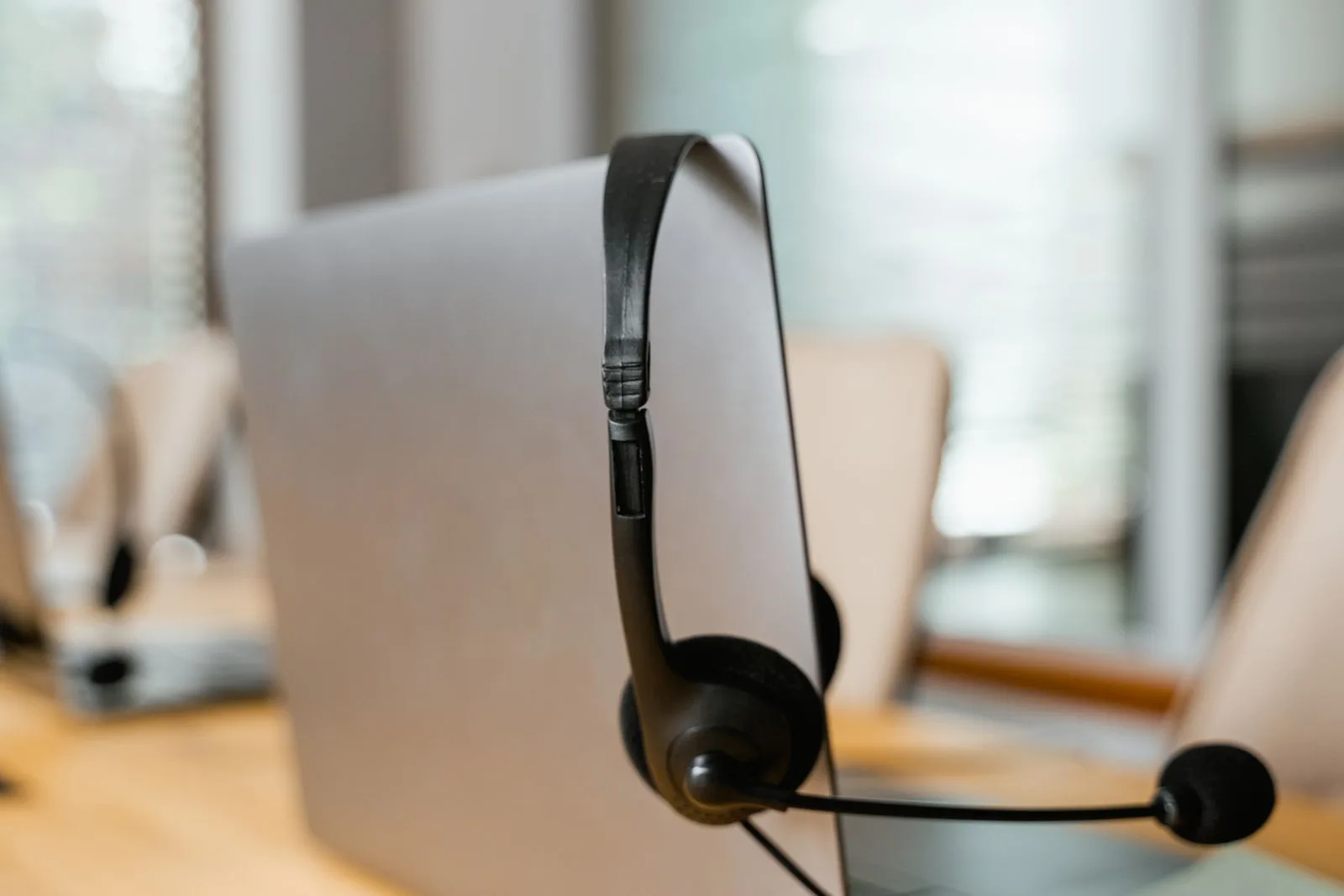 A telephone headset hooked over the lid of a laptop on an otherwise empty desk