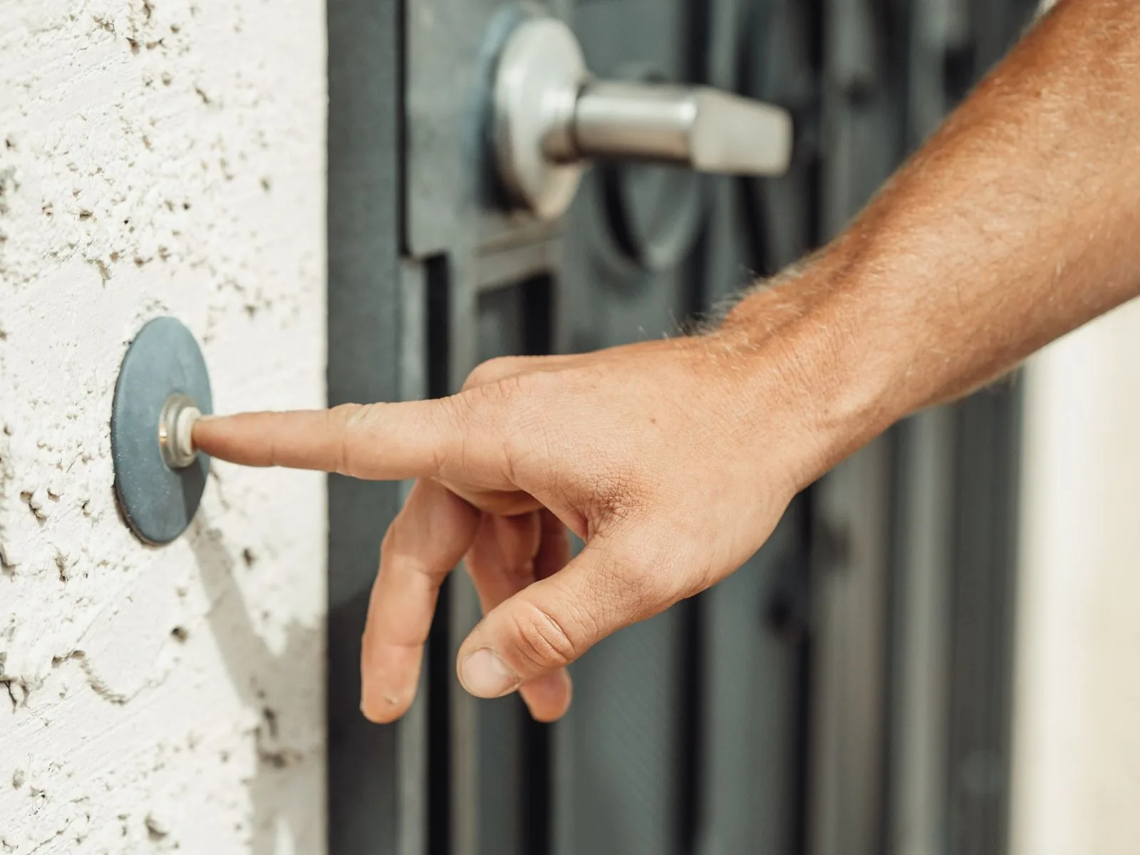 A hand reaching in to press a doorbell beside a residential front door