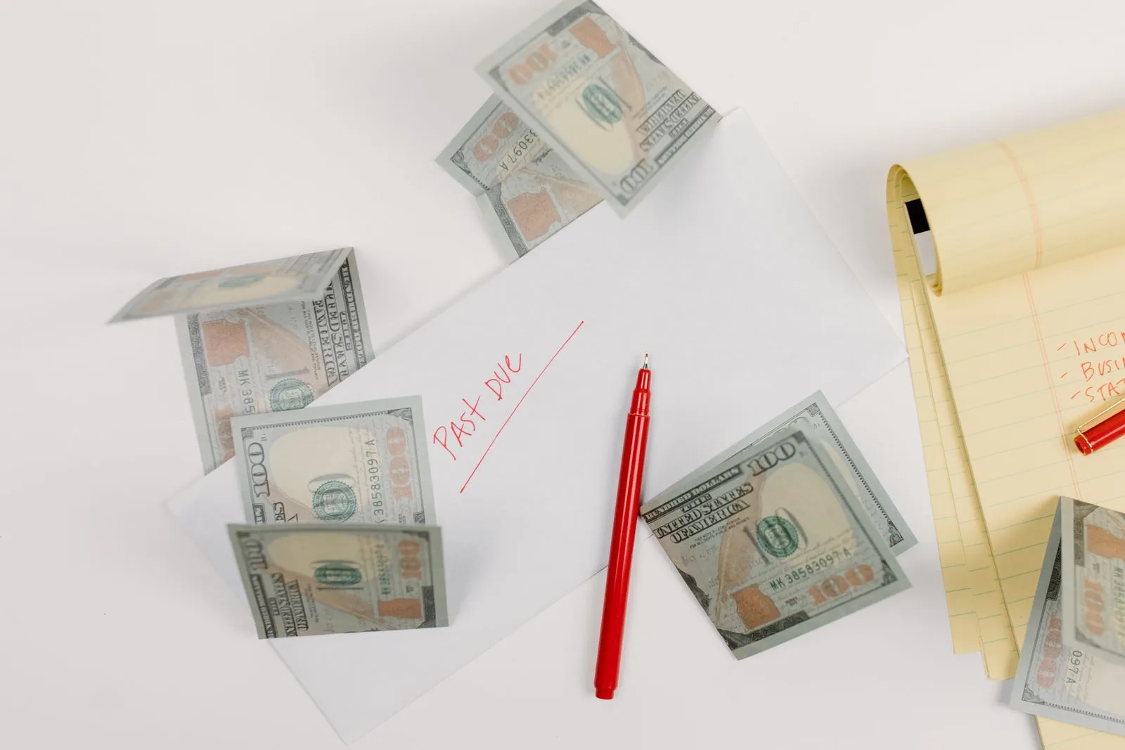 An envelope marked past due in red pen with hundred dollar bills scattered around it